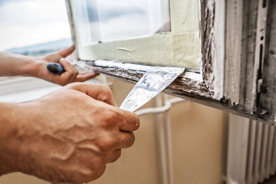 Technician scraping old paint from a wood window sill during restoration