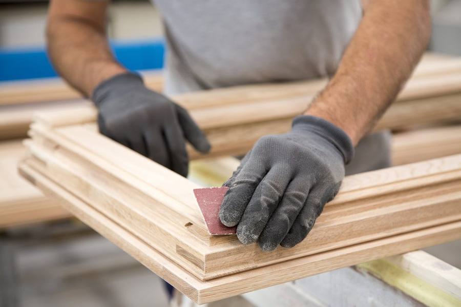 Gloved technician hand-sanding a wood window frame in the workshop before refinishing